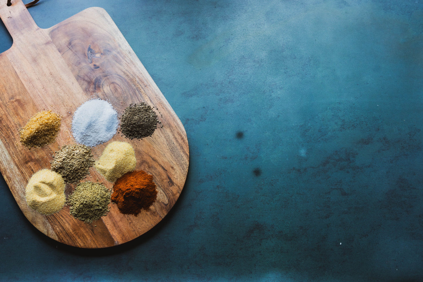 Wooden cutting board with various spices on a blue background