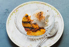 Glass bowl with grilled peaches using the Ember spice blend, and vanilla ice cream on a decorative plate with a spoon.