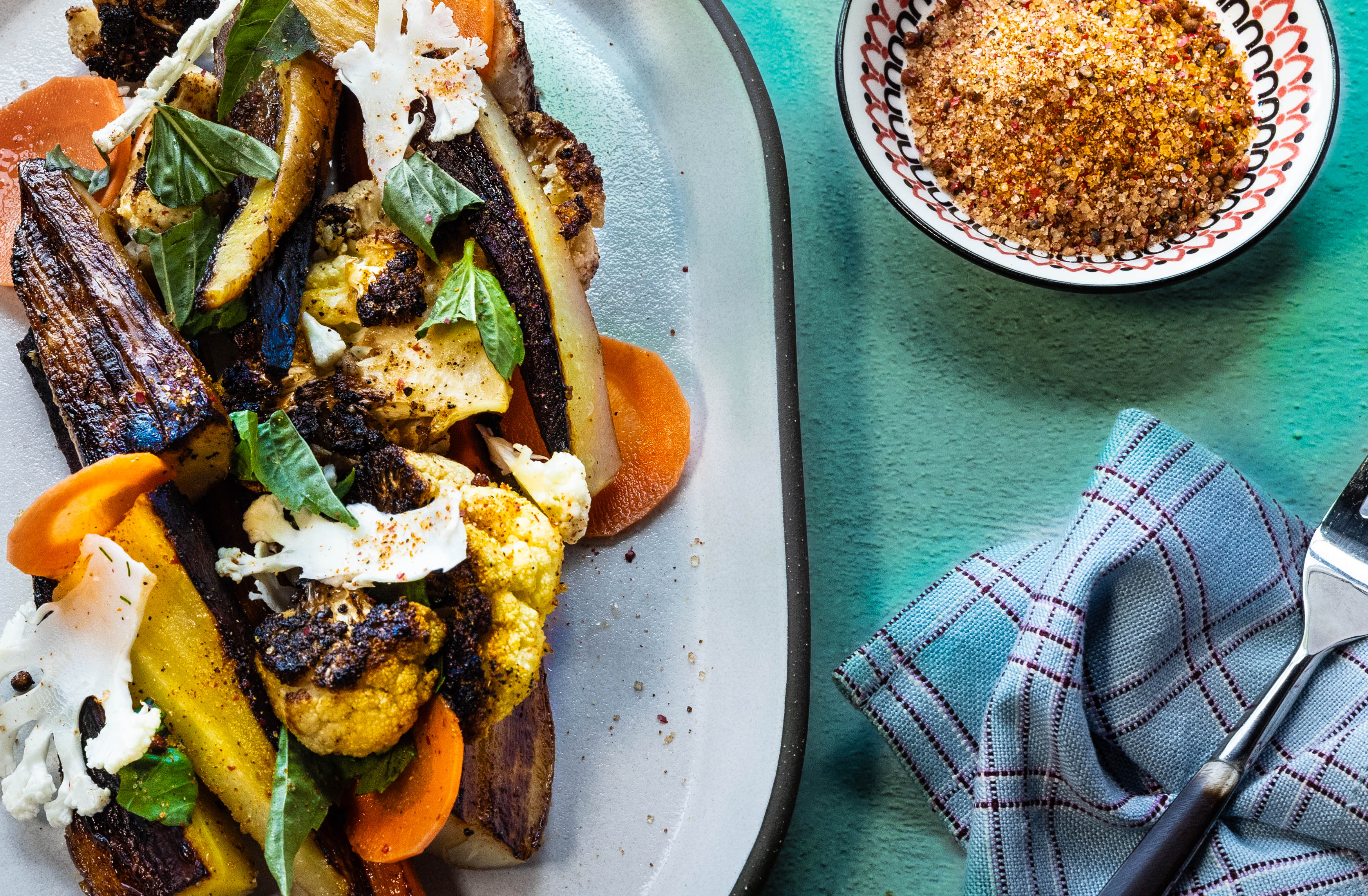 Plated dish of roasted vegetables seasoned with the House Blend, with a side of bread on a teal tablecloth.